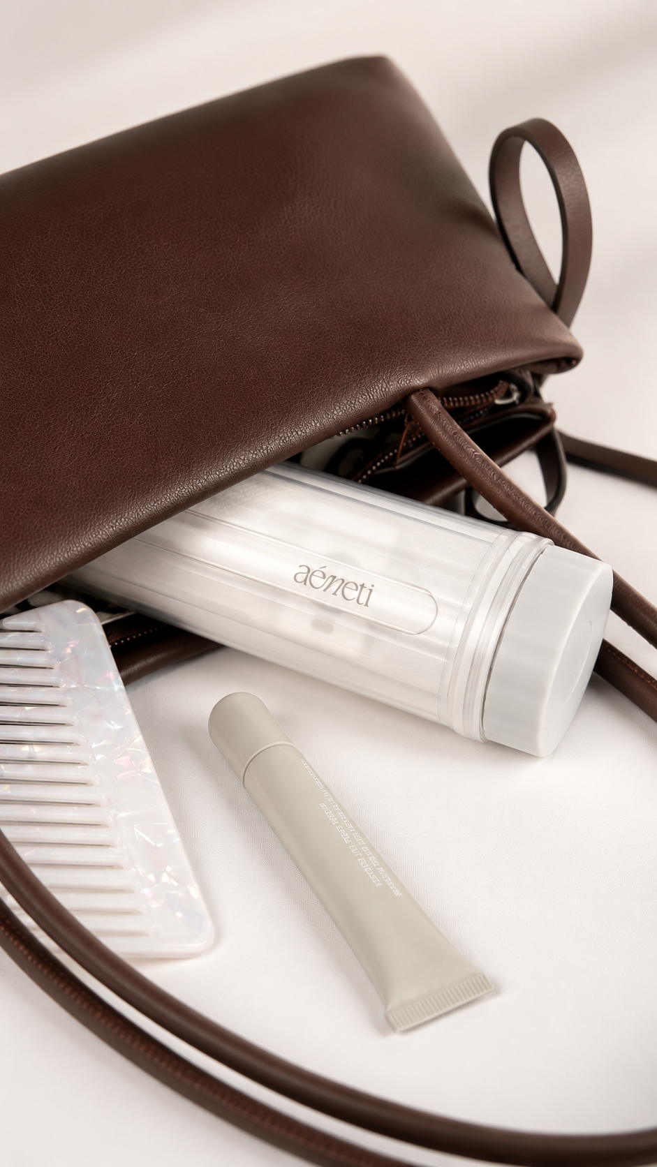 A brown leather clutch bag shown open with several travel-sized toiletry items arranged inside on a white surface, including a clear cylindrical bottle, a small tube, and a white comb.